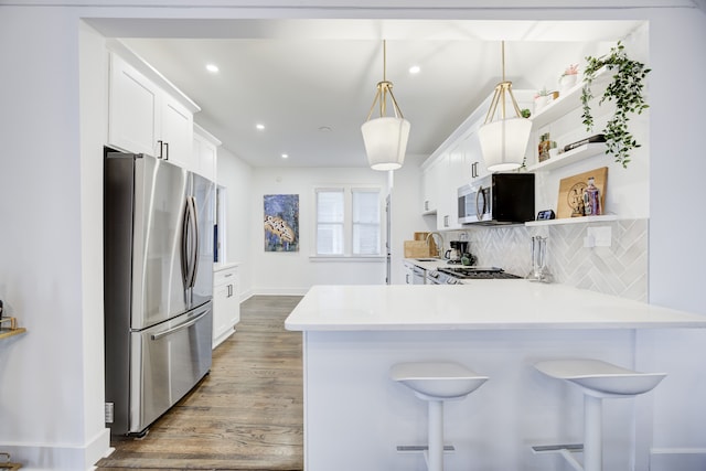 kitchen featuring a kitchen bar, kitchen peninsula, stainless steel appliances, decorative light fixtures, and white cabinets