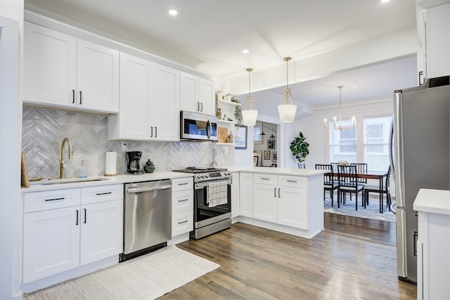 kitchen with kitchen peninsula, appliances with stainless steel finishes, sink, white cabinetry, and hanging light fixtures