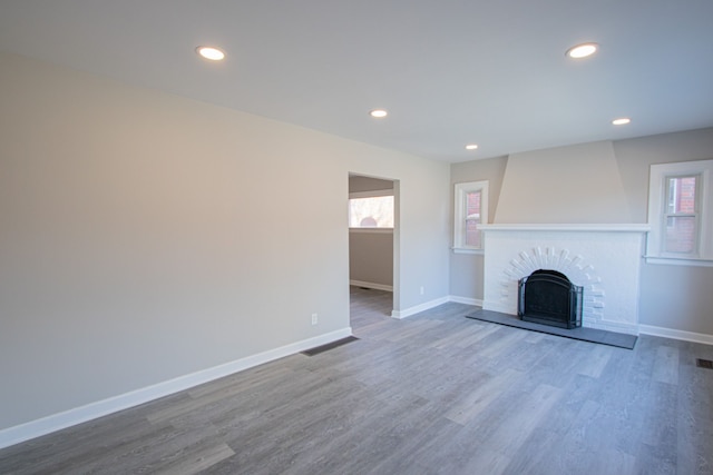 unfurnished living room featuring hardwood / wood-style floors, a healthy amount of sunlight, and a brick fireplace