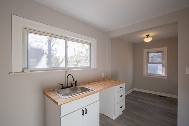 kitchen with butcher block countertops, dark hardwood / wood-style flooring, white cabinetry, and sink