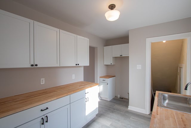 kitchen featuring butcher block countertops, white cabinetry, sink, and light wood-type flooring