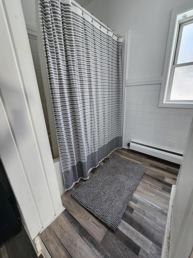 bathroom featuring shower / tub combo, hardwood / wood-style flooring, a baseboard radiator, and tile walls