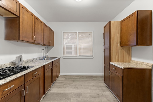 kitchen featuring light stone countertops, light hardwood / wood-style floors, black gas cooktop, and sink