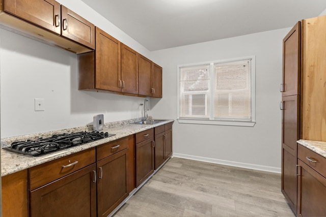 kitchen featuring light stone counters, black gas stovetop, light wood-type flooring, and sink