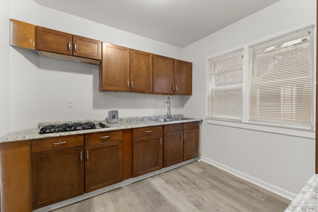 kitchen featuring light wood-type flooring, gas stovetop, light stone counters, and sink