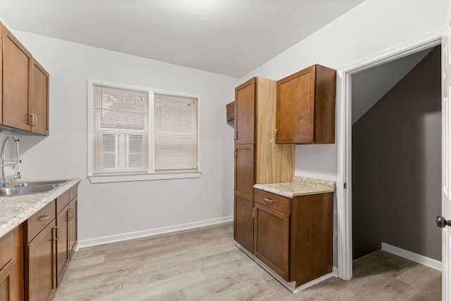 kitchen with light stone counters, light wood-type flooring, and sink