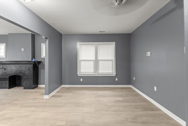 unfurnished living room featuring ceiling fan, a healthy amount of sunlight, light hardwood / wood-style floors, and a brick fireplace