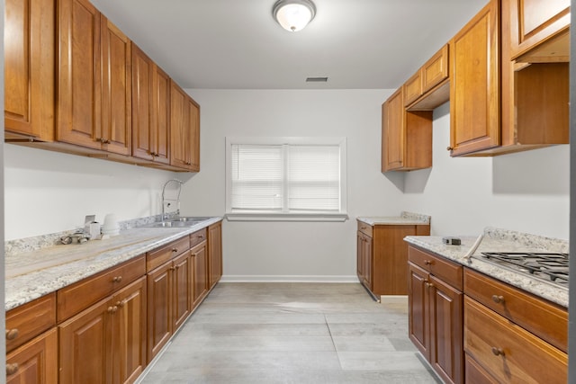 kitchen featuring light stone counters, sink, light wood-type flooring, and stainless steel gas cooktop