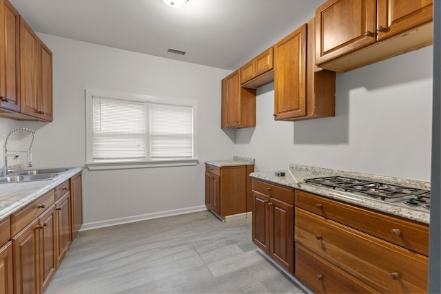 kitchen with light stone countertops, stainless steel gas stovetop, and sink