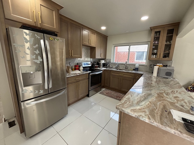 kitchen with sink, light stone counters, backsplash, light tile patterned floors, and appliances with stainless steel finishes