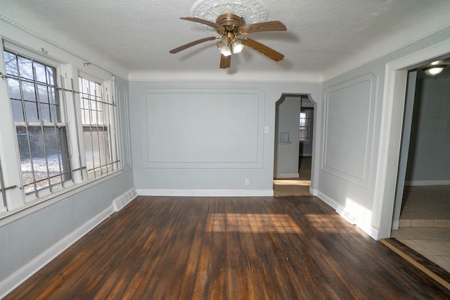 unfurnished room with a textured ceiling, ceiling fan, dark hardwood / wood-style flooring, and plenty of natural light