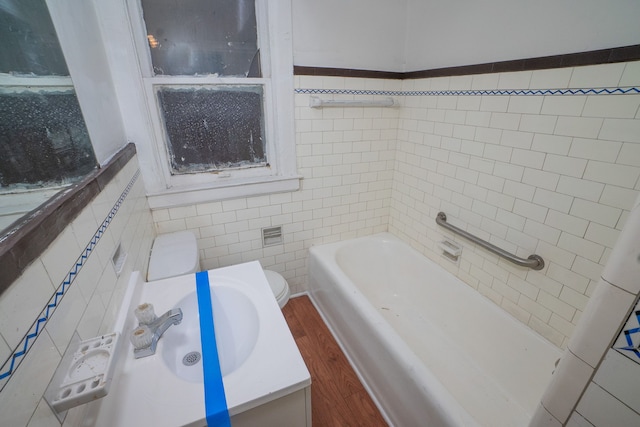 bathroom with toilet, a bathtub, vanity, tile walls, and hardwood / wood-style flooring