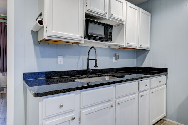 kitchen with white cabinetry, dark stone countertops, and sink