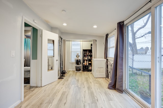 corridor with plenty of natural light, light hardwood / wood-style floors, and vaulted ceiling