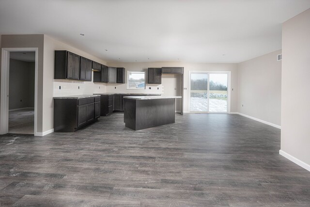 kitchen with decorative backsplash, dark brown cabinetry, a kitchen island, and dark wood-type flooring