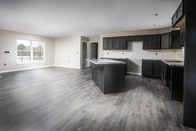 kitchen featuring hardwood / wood-style floors, a kitchen island, light stone countertops, and backsplash