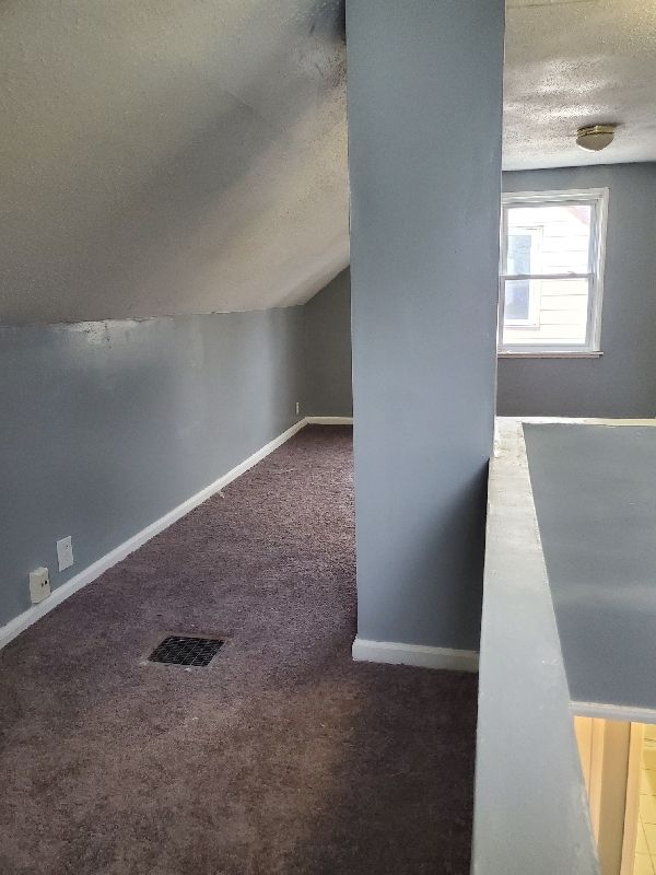 bonus room featuring dark carpet, a textured ceiling, and vaulted ceiling