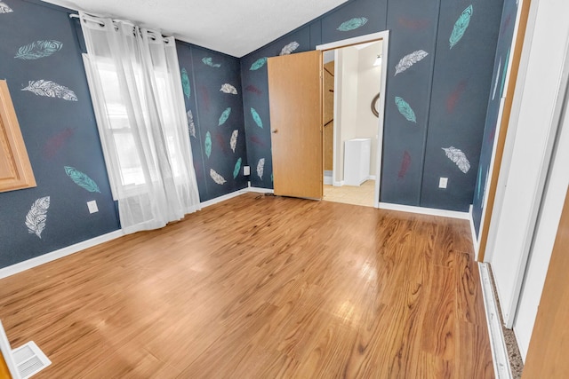 unfurnished bedroom with a textured ceiling, lofted ceiling, and light wood-type flooring