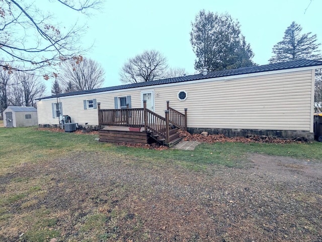 back of house with central air condition unit, a lawn, a deck, a storage shed, and an outdoor structure