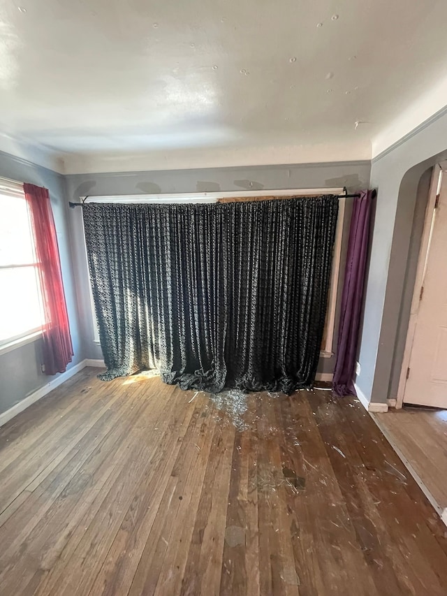 empty room with baseboards, arched walkways, and hardwood / wood-style floors