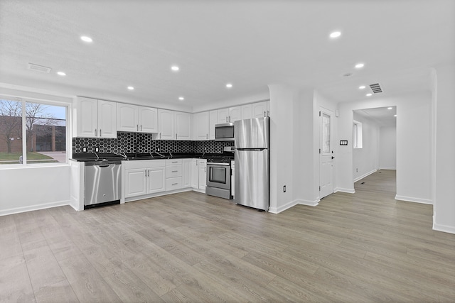 kitchen featuring tasteful backsplash, light hardwood / wood-style flooring, white cabinets, and stainless steel appliances