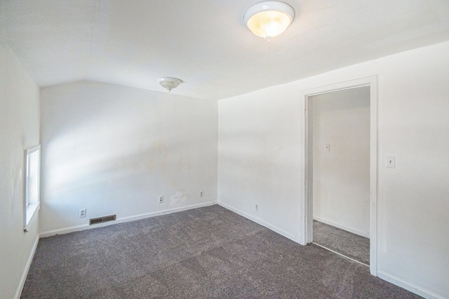 spare room featuring vaulted ceiling and dark colored carpet