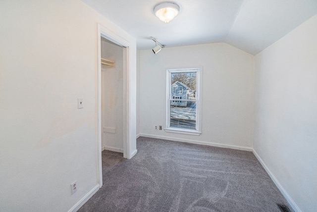 unfurnished room with vaulted ceiling and dark colored carpet