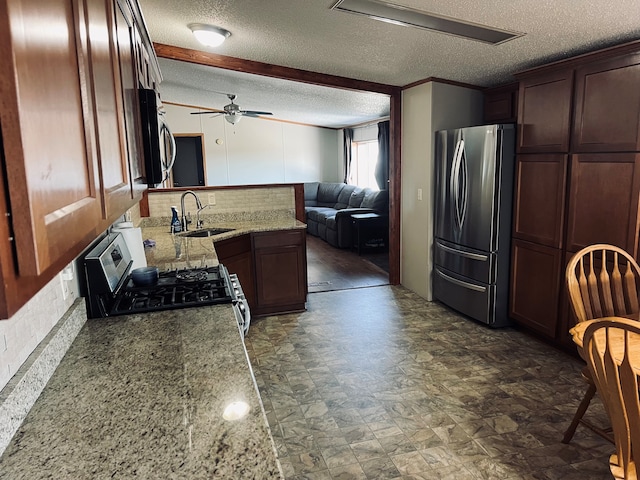 kitchen featuring light stone countertops, appliances with stainless steel finishes, a textured ceiling, ceiling fan, and sink