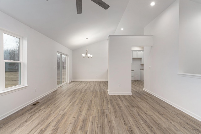 unfurnished living room featuring a healthy amount of sunlight, lofted ceiling, ceiling fan with notable chandelier, and light wood-type flooring