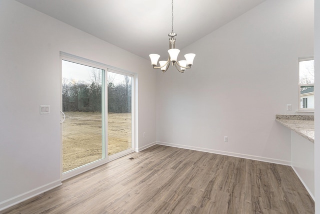 unfurnished dining area with hardwood / wood-style flooring, vaulted ceiling, and a notable chandelier