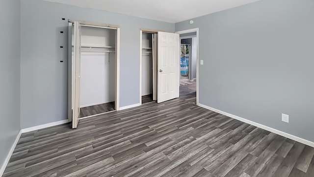 unfurnished bedroom with two closets and dark hardwood / wood-style floors