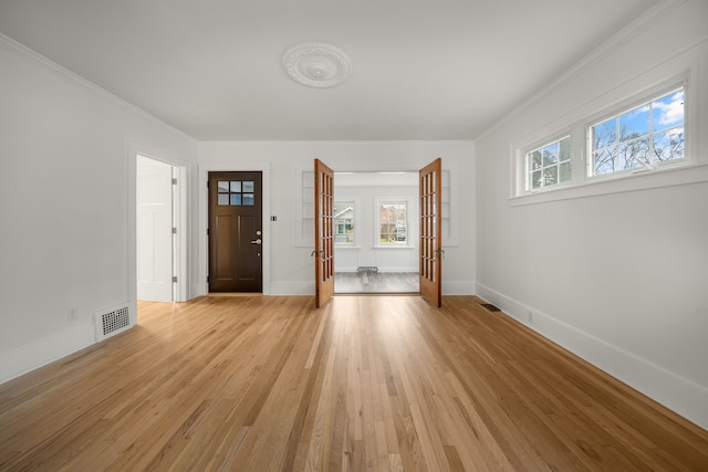 empty room featuring crown molding, french doors, a healthy amount of sunlight, and light wood-type flooring