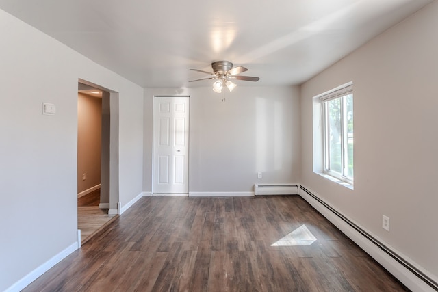 empty room with dark hardwood / wood-style floors, ceiling fan, and a baseboard heating unit