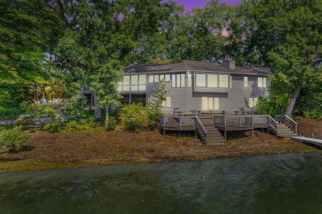 back house at dusk with a deck with water view