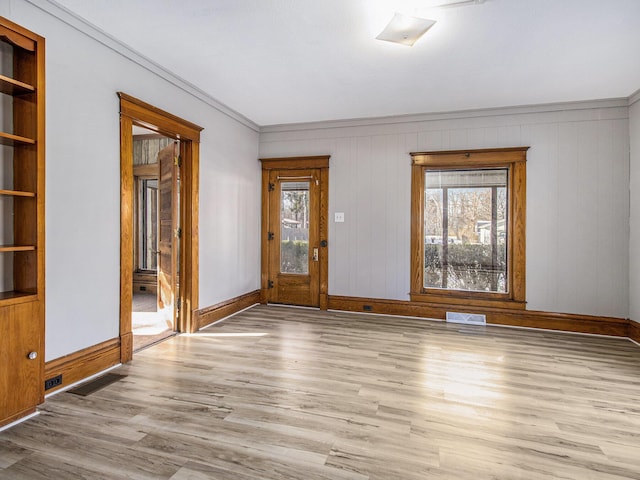 unfurnished room featuring built in shelves, crown molding, and light hardwood / wood-style flooring