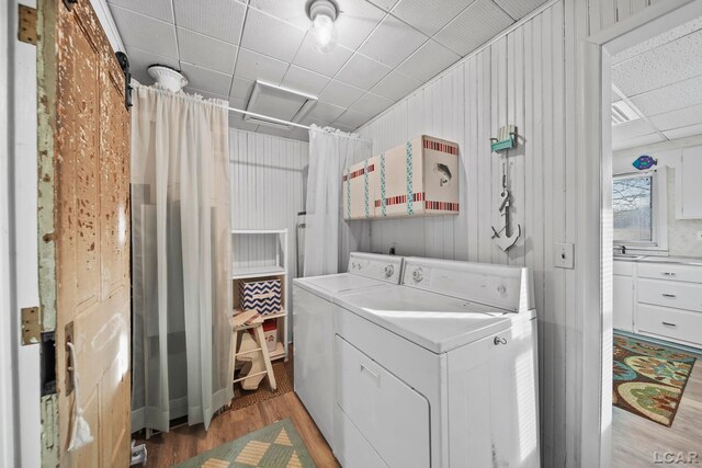 laundry area with wood walls, wood-type flooring, and separate washer and dryer