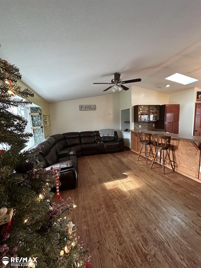 living room featuring dark hardwood / wood-style flooring, vaulted ceiling with skylight, and ceiling fan