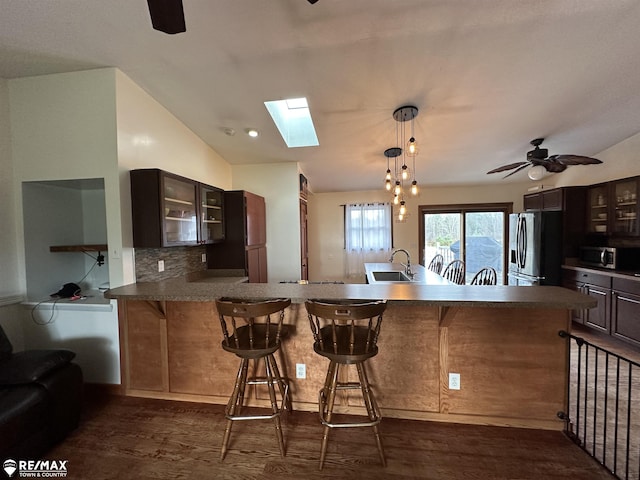 kitchen featuring dark wood-type flooring, a kitchen breakfast bar, stainless steel appliances, vaulted ceiling with skylight, and kitchen peninsula