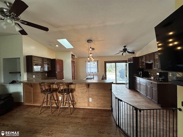 kitchen with dark brown cabinets, vaulted ceiling with skylight, a kitchen bar, decorative backsplash, and kitchen peninsula