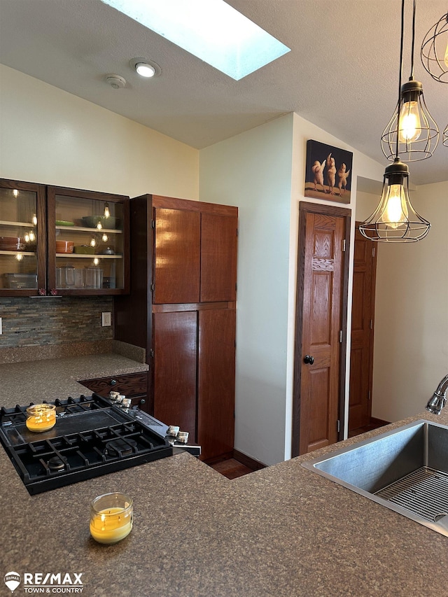 kitchen with sink, stovetop, dark brown cabinets, lofted ceiling with skylight, and tasteful backsplash