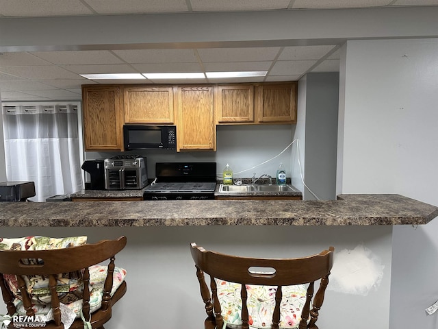 kitchen with a drop ceiling, a kitchen bar, sink, and black appliances