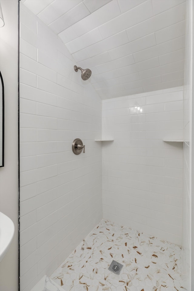 bathroom with a tile shower and lofted ceiling