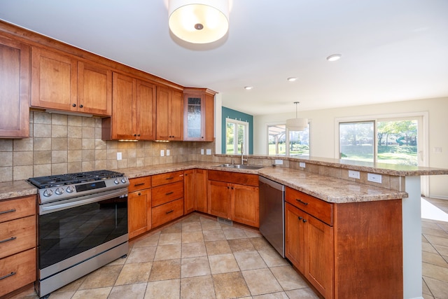 kitchen with sink, light stone counters, kitchen peninsula, pendant lighting, and appliances with stainless steel finishes