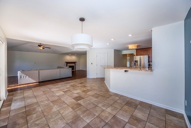 kitchen with pendant lighting, sink, stainless steel fridge, light stone counters, and kitchen peninsula