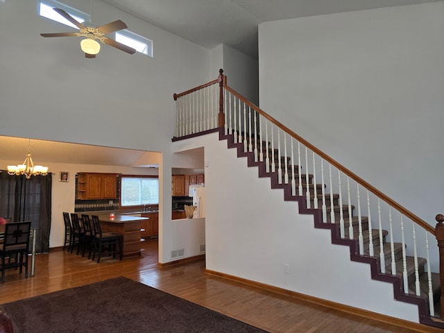 staircase featuring sink, high vaulted ceiling, wood-type flooring, and ceiling fan with notable chandelier