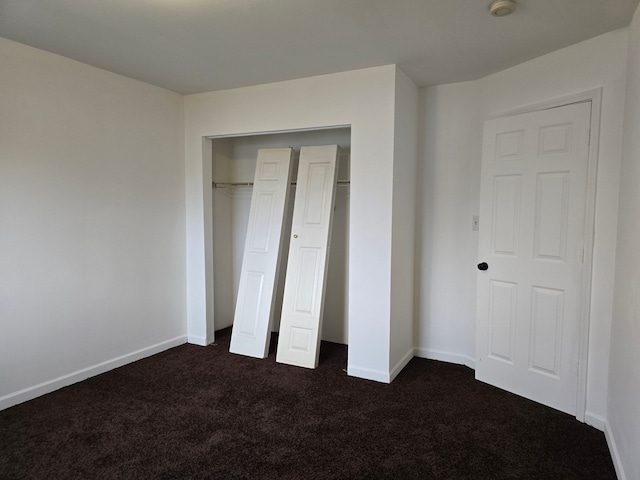 unfurnished bedroom with dark carpet and a closet