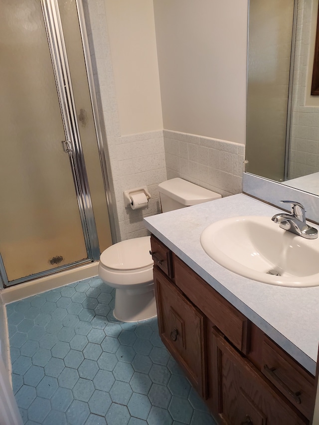 bathroom featuring vanity, toilet, walk in shower, and tile walls