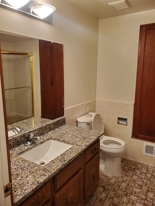 bathroom with vanity, toilet, a shower with shower door, and tile walls