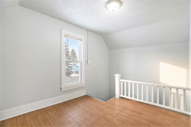 additional living space featuring a textured ceiling, lofted ceiling, and hardwood / wood-style flooring