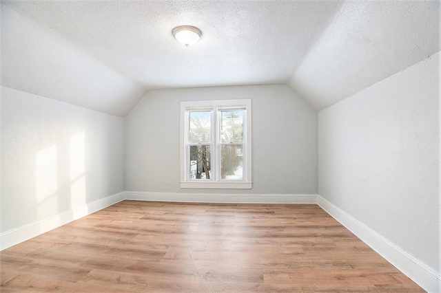 additional living space featuring a textured ceiling, light hardwood / wood-style flooring, and vaulted ceiling